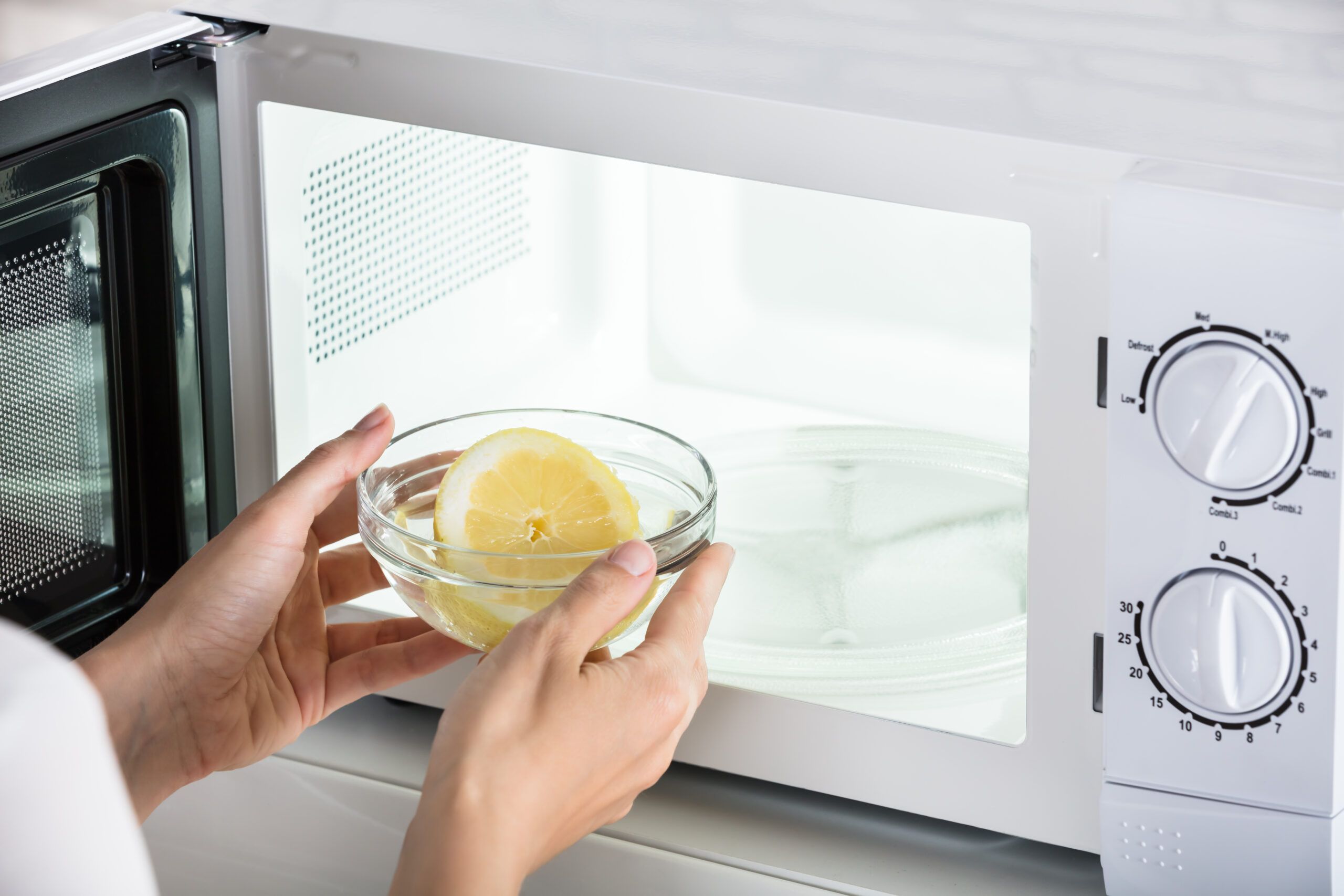 Close-up Of Woman Putting Bowl Of Slice Lemon In Microwave Oven