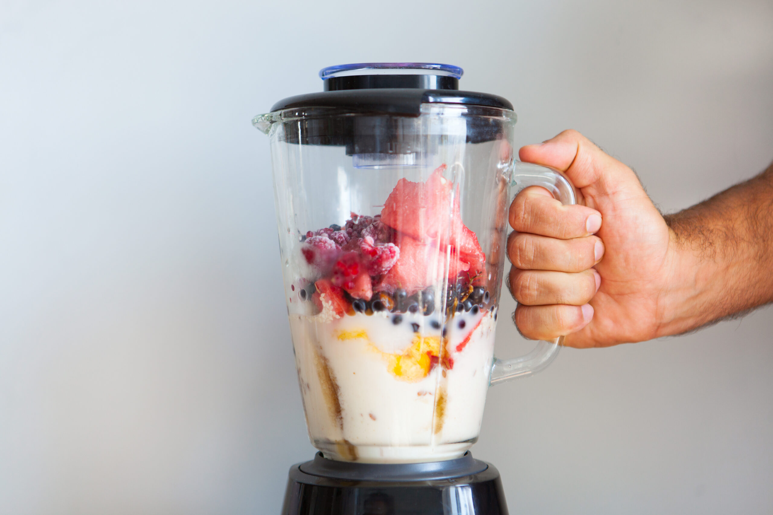 Men's hand hold blender filled with fresh whole fruits for making a smoothie or juice. Closeup