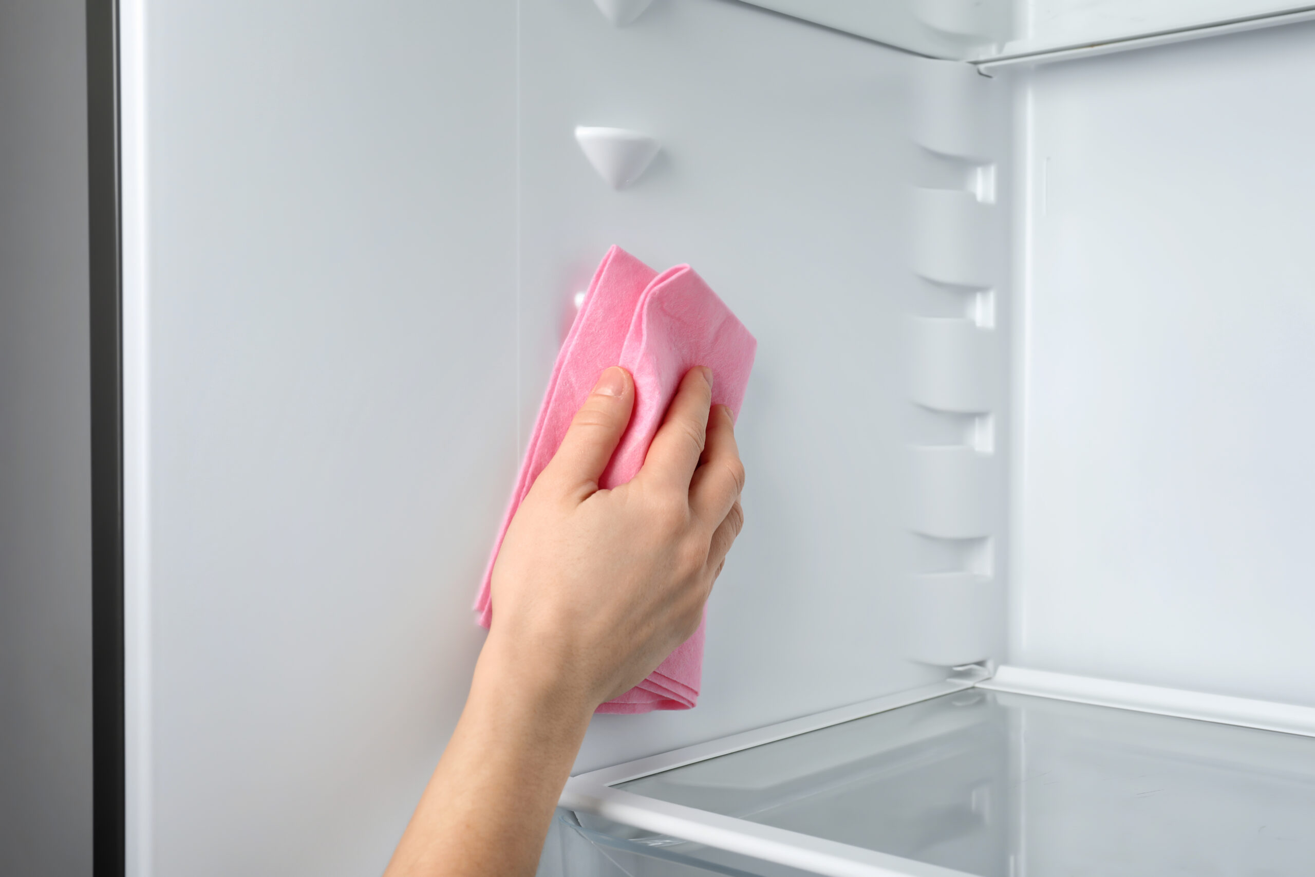 Woman cleaning refrigerator with pink cloth, closeup
